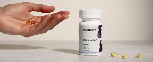 A hand holding two CBD capsules next to a bottle of Medterra Daily Relief CBD Capsules.