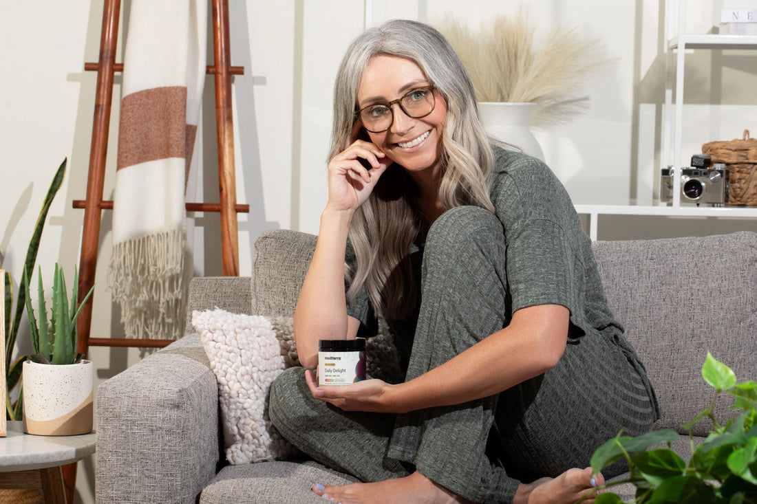Smiling woman on a couch holding a jar labeled medterra Daily Delight
