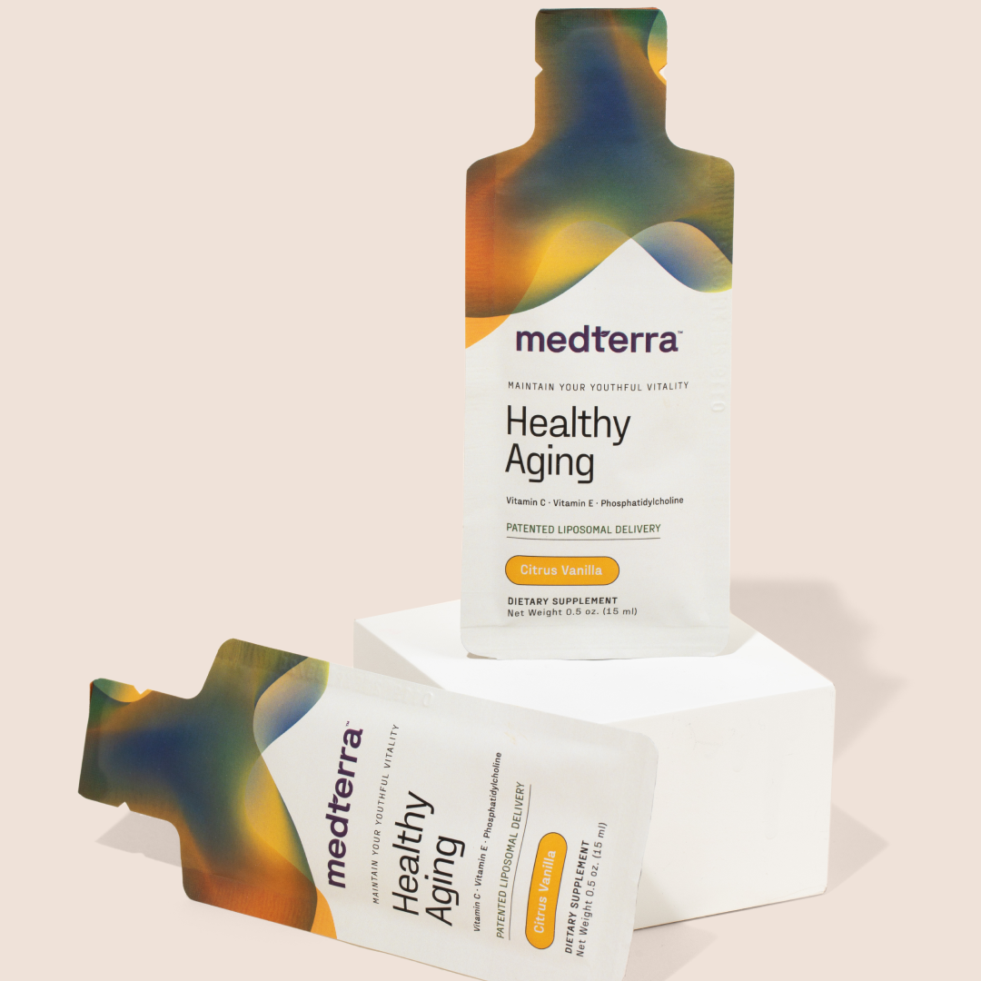 Two sachets of the Healthy Aging supplement from Medterra are displayed against a light background. One upright sachet is positioned on a white block, while the other lies flat. They feature a colorful design with text detailing the product's ingredients, including Vitamin C and Citrus Vanilla, promoting immune health.