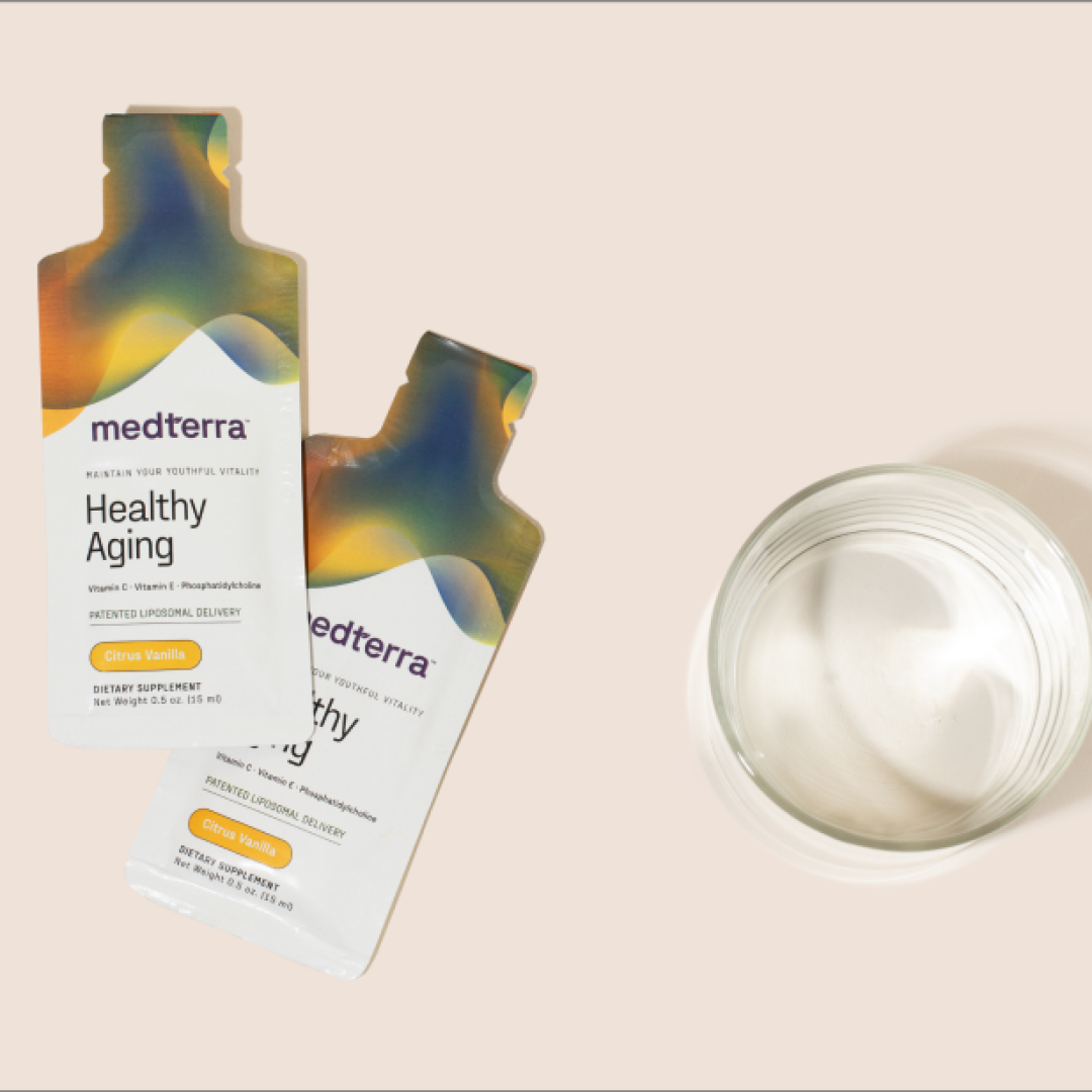 The image depicts two packets of Medterra's Healthy Aging dietary supplement with advanced liposomal technology positioned beside an empty glass. The packets, labeled "Citrus Vanilla" flavor, exhibit a vibrant gradient design and are set against a light beige background.