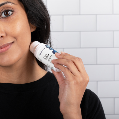 A person with long dark hair and a black shirt is applying Medterra's Pain Relief Roll-On to the side of their neck, against a backdrop of white tiles. The label on the bottle reads "Pain Relief" and contains 1000mg CBD for joint pain relief.
