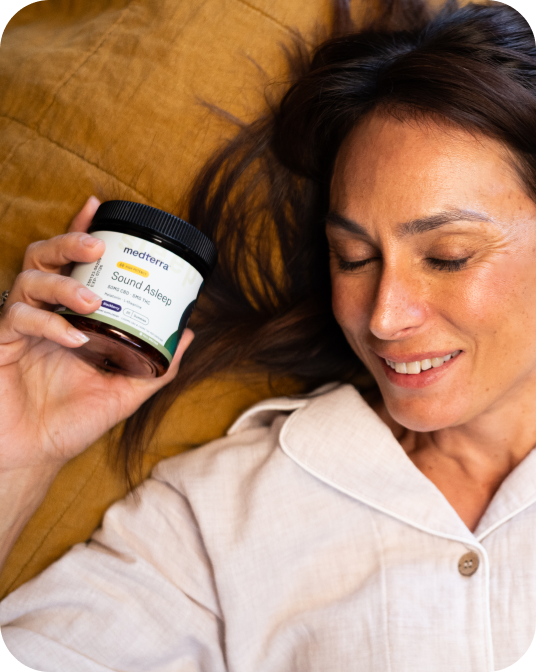 Woman reclining on a pillow in pajamas, eyes closed, holding a jar labeled medterra Sound Asleep.