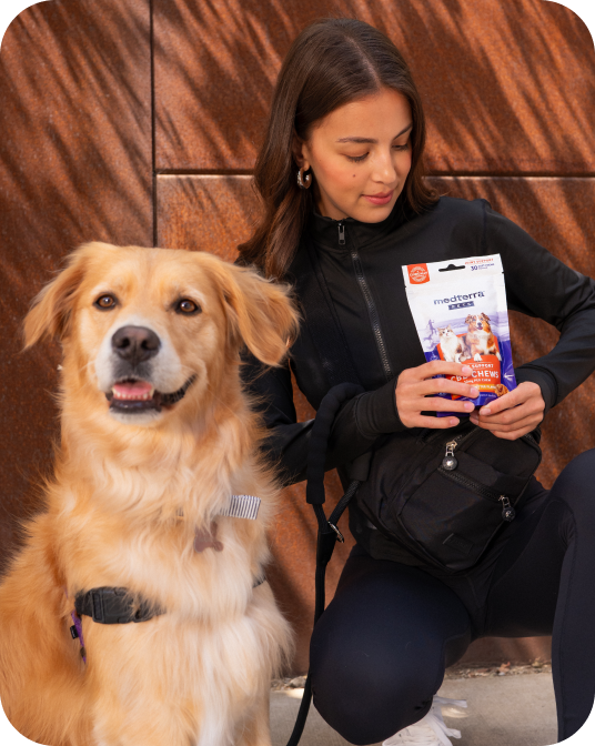 Woman kneeling with golden retriever, holding a medterra CHEWS dog supplement pouch