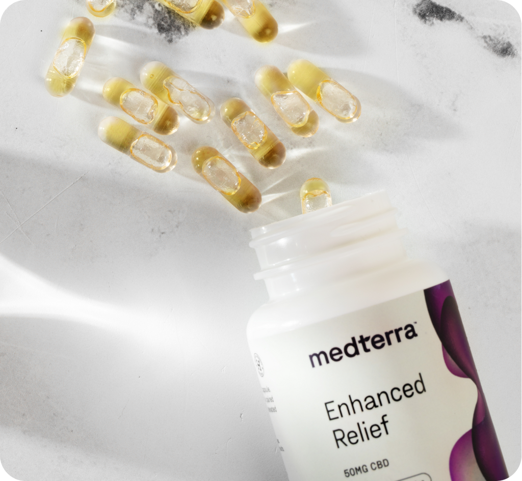 A white bottle labeled "Medterra Enhanced Relief 50mg CBD" lies open on a marble surface, with several yellowish, translucent CBD pills spilling out beside it. The bottle, designed with a purple motif, promises to relieve stress effectively.
