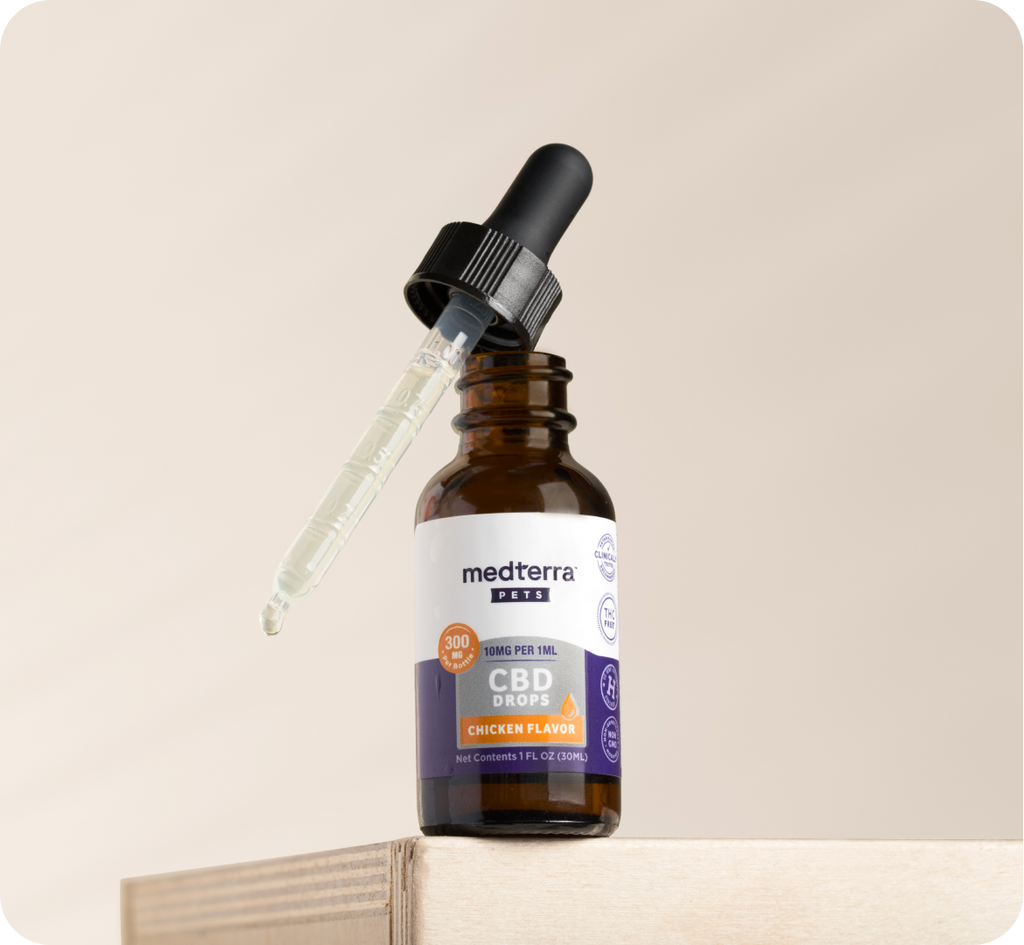 A small bottle of Medterra Pets CBD drops labeled "Chicken Flavor," with a dropper resting on top. The brown bottle, capped in black and labeled in white, contains 150 mg per ml of CBD and organic MCT Oil. Perfect for a restless cat or dog, it sits on a wooden surface against a neutral background.