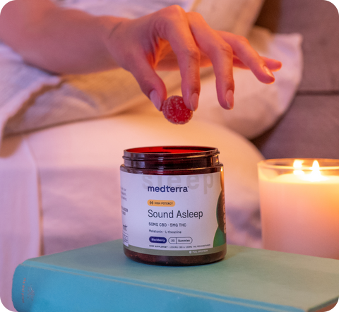 Hand placing a raspberry on a jar of Medterra Sound Asleep supplement labeled 50MG CBD - 5MG THC, Melatonin, L-theanine, with a lit candle in the background.