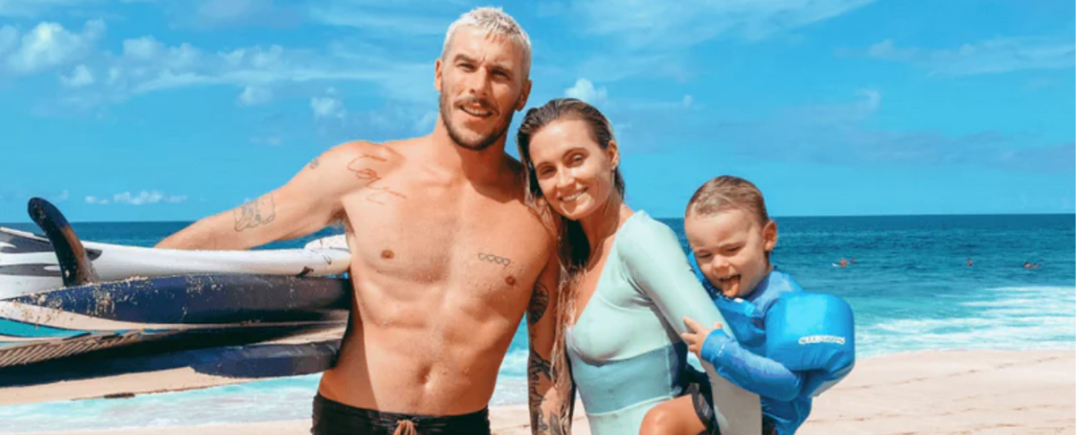 Alana Blanchard with her partner and child at the beach, holding surfboards