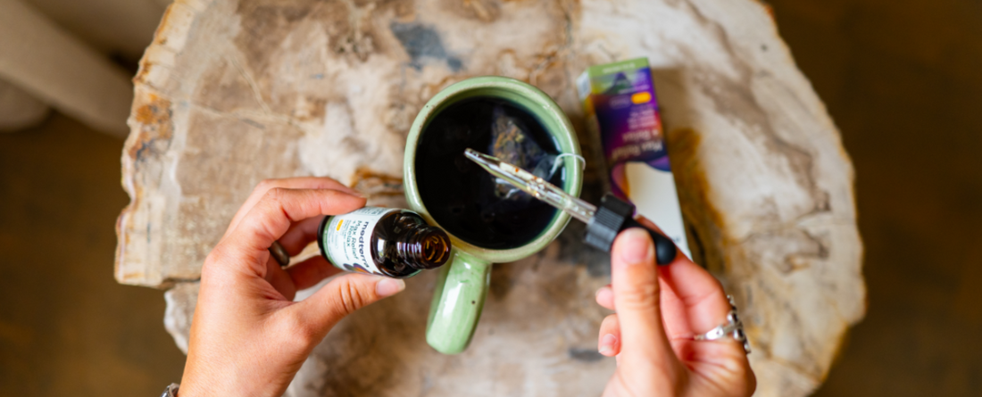 Person holding a dropper over a green mug with CBD oil bottle nearby