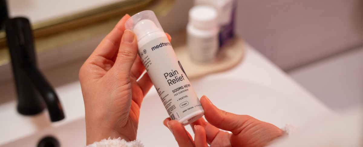A person holding a bottle of Medterra Pain Relief cream in a bathroom setting.