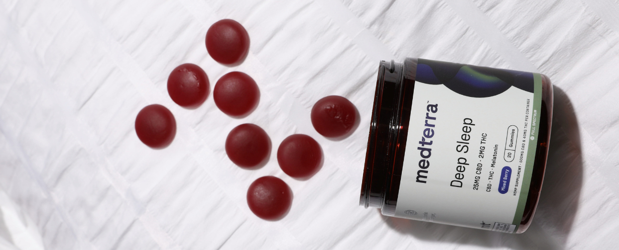 A jar of Medterra Deep Sleep CBD gummies with red gummies scattered around it.