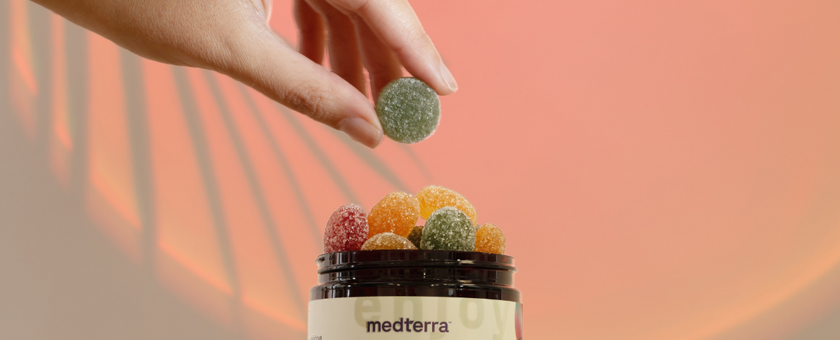 A hand holding a green gummy above a jar filled with colorful CBD gummies.