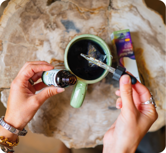 Hands holding Medterra Max Relief tincture bottle and dropper over a green cup with tea on a wooden table