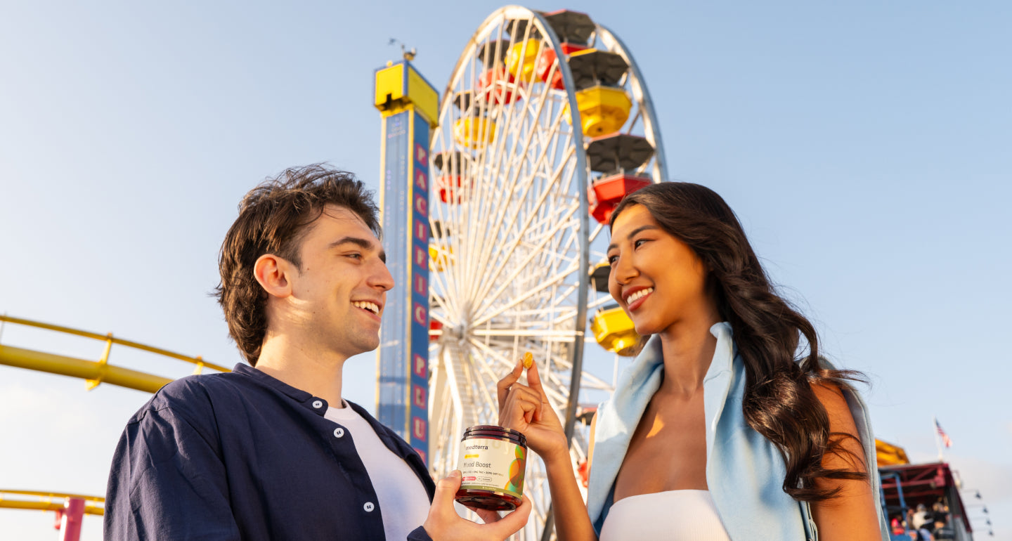 Young couple sharing a gummy near a Ferris wheel at PACIFIC PIER, one holding a jar