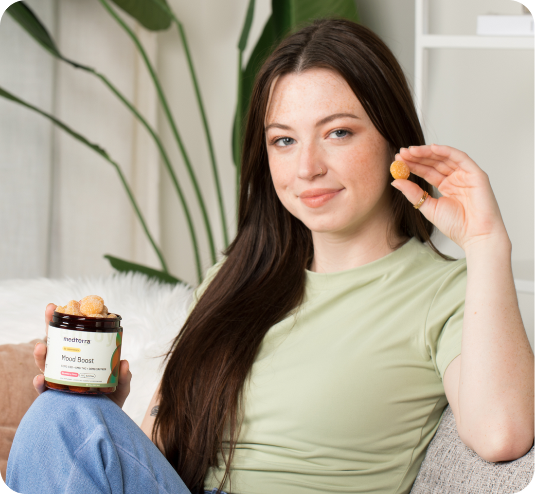 Young woman holding a jar labeled medterra Mood Boost and holding a single yellow CBD gummy.