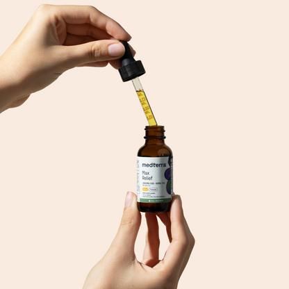 A hand holds a brown bottle labeled "Medterra Max Relief Full Spectrum CBD Oil," with a dropper full of yellow liquid held above it. Crafted from organically grown hemp, this advanced tincture ensures premium quality relief. The background is solid beige.