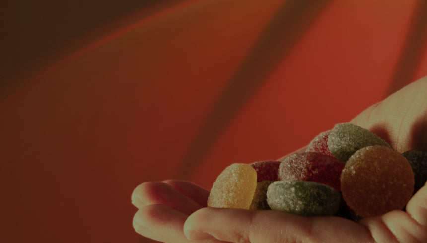 A close-up of a hand holding assorted colorful Medterra CBD gummies. The background is a gradient of warm red and orange hues, creating a vibrant and cozy atmosphere.