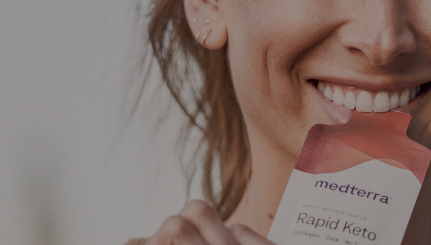 A person smiles while holding a "Medterra Rapid Keto" packet near their mouth. The focus is on the person’s mouth and the packet, highlighting the product. The background appears blurred, emphasizing the main subjects.