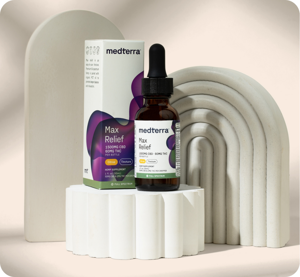 A bottle of Medterra Max Relief Full Spectrum CBD oil, sourced from organically grown hemp, is displayed in front of its packaging. The bottle has a dropper top and is labeled "1500mg CBD 0.9mg THC." The items are set against a geometric, sculptural background of white, arch-shaped elements on a neutral backdrop.