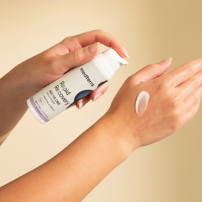 A person’s hands are depicted applying Medterra's Rapid Recovery CBD Cream to the back of one hand. A small amount of the THC-free product has been dispensed onto the skin. The background is a light, neutral color.