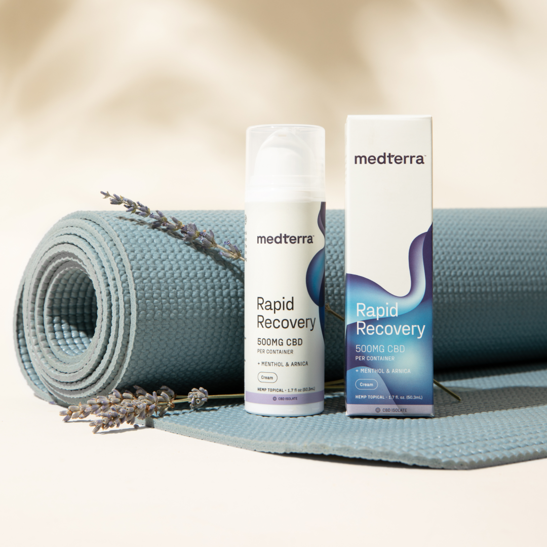 A bottle and box of Medterra Rapid Recovery CBD Cream (500mg) with menthol and arnica are placed beside a blue yoga mat. Two sprigs of lavender lie on the mat near the THC-free joint and muscle support products. The items are set against a neutral background.