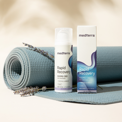 A bottle and box of Medterra Rapid Recovery CBD Cream (500mg) with menthol and arnica are placed beside a blue yoga mat. Two sprigs of lavender lie on the mat near the THC-free joint and muscle support products. The items are set against a neutral background.
