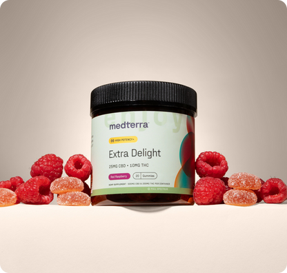 A jar of Medterra Extra Delight 10mg THC Gummies sits among fresh raspberries and sugar-coated gummies against a neutral background, showcasing their high-potency blend of CBD and THC.