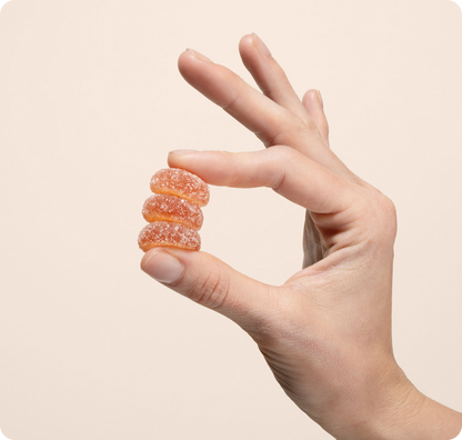A hand holds a stack of four orange, sugar-coated Medterra Extra Delight 10mg THC Gummies between the thumb and index finger against a plain light background.