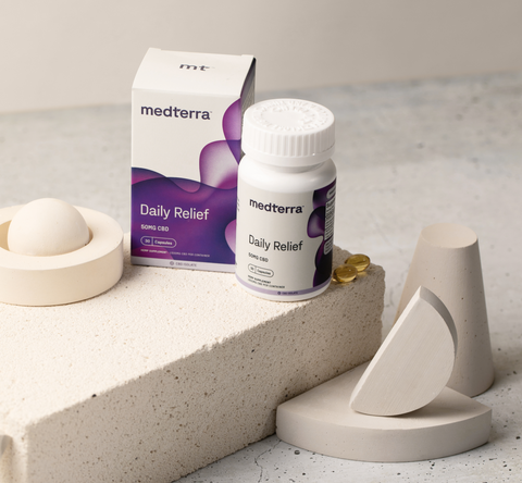 A product photo featuring Medterra's Daily Relief CBD capsules with the box and bottle prominently displayed. The scene includes abstract beige geometric shapes and three yellow capsules to the side, all set against a neutral background, highlighting Medterra CBD Isolate for effective relief.