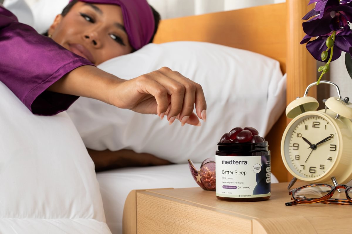 Woman in bed reaching for a jar of Medterra Better Sleep gummies on her nightstand